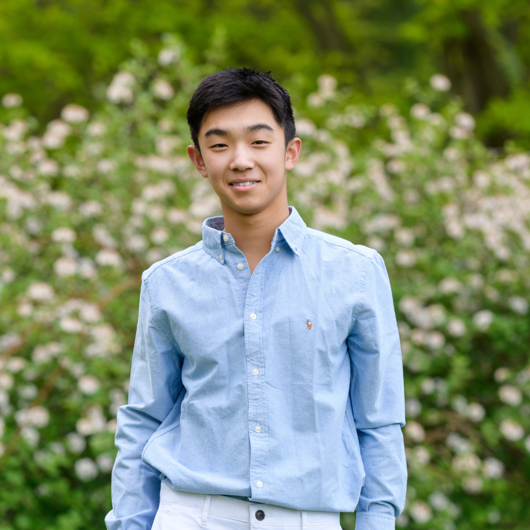 Cary Wang in blue shirt standing in front of bush