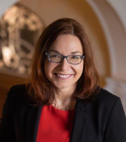 Woman with shoulder-length brown hair wearing glasses and smiling